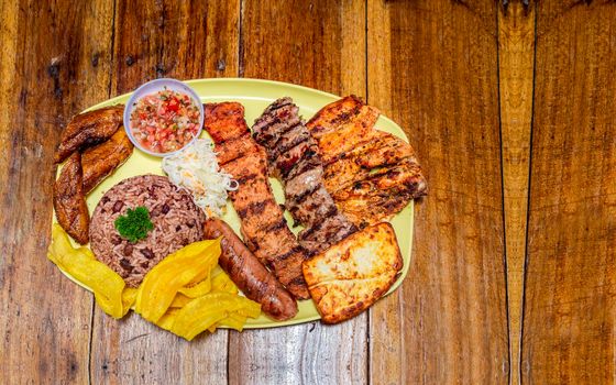 roast beef with rice, fried cheese and tomato salad, Nicaraguan food served on wooden table, plate with assorted types of grilled meats on wooden table