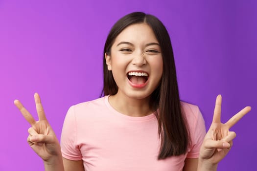 Close-up carefree smiling positive asian girl celebrating pride laughing joyfully, show peace sign victory, joking, stand amused entertained, attend funny event, celebrate b-day, photographing.