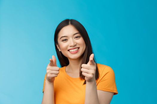 Cheerful friendly good-looking modern asian woman show finger pistols joyfully, pointing camera, smiling broadly, congratulate friend good job, encourage you keep working, stand blue background.