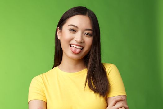 Close-up silly cute flirty asian girl fool around childish, playfully communicate boyfriend, show tongue smiling broadly, cross hands chest casually, enjoy summer holidays, green background.