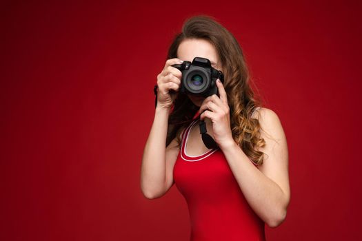 A beautiful bright woman with a camera in her hands. A woman on a red background in a red swimsuit poses with a camera