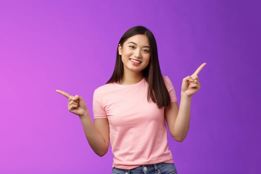 Charismatic relaxed cute asian woman short haircut pointing sideways introduce variety choices, showing left and right products, smiling joyfully, easily making decision, stand purple background.