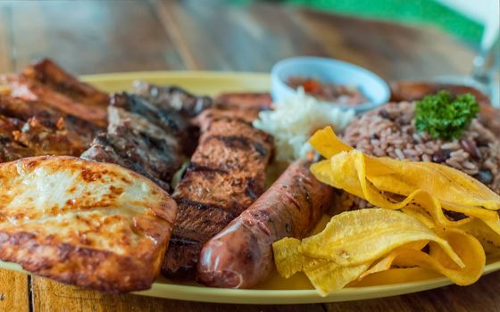 roast beef with rice, fried cheese and tomato salad, Nicaraguan food served on wooden table, plate with assorted types of grilled meats on wooden table