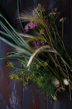 Fresh green onion, dill flowers, rye spikelets and yarrow pink flowers on dark blue table, summer concept, flat lay, selective focus