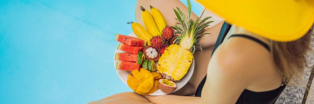 Young woman relaxing and eating fruit plate by the hotel pool. Exotic summer diet. Photo of legs with healthy food by the poolside, top view from above. Tropical beach lifestyle. BANNER, LONG FORMAT