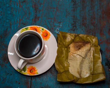 Stuffed tamale served on wooden table, stuffed tamale on banana leaf served with a cup of coffee on wooden table, typical nicaragua food