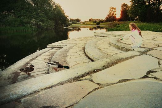 little girl with her mother feeding the ducks near the lake in the Park on a summer day