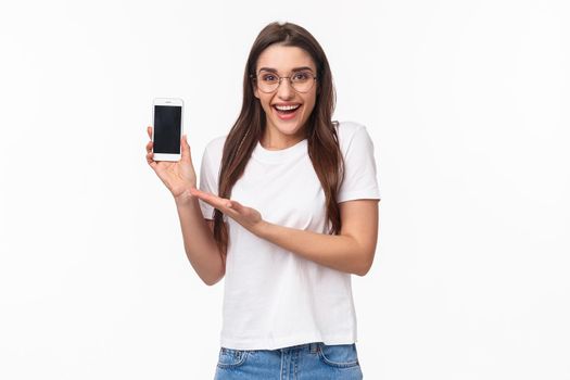 Communication, technology and lifestyle concept. Portrait of lovely hipster girl in glasses, introduce new application, own mobile app, recommend upload online shopping store, hold smartphone.
