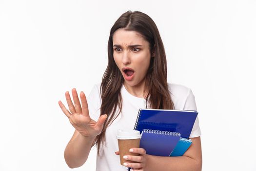Education, university and studying concept. Close-up portrait of shocked young woman holding notebooks and learning material staring at her hand with shock as she broke her finger, need go salon.