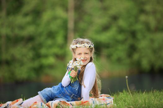 cute little girl in a wreath and a bouquet of wildflowers on a picnic in the woods on a Sunny day