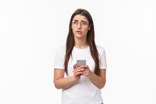 Communication, technology and lifestyle concept. Portrait of troubled and concerned young woman worried for friend, sending text message if shes okay and thinking, look up nervous, hold mobile phone.
