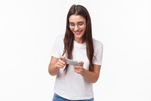 Communication, technology and lifestyle concept. Portrait of charismatic funny and happy young carefree girl in glasses, playing awesome racing or arcade game on mobile phone, enjoy using app.