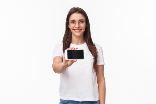 Communication, technology and lifestyle concept. Portrait of young charming woman in glasses and t-shirt, showing smartphone screen horizontal, introduce game or application.
