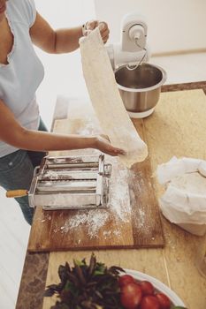 A woman sends rolled out noodle dough to a noodle slicer against the background of a dough mixer