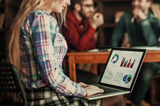 sales Manager working on laptop with a marketing report on the background of business team in a modern office