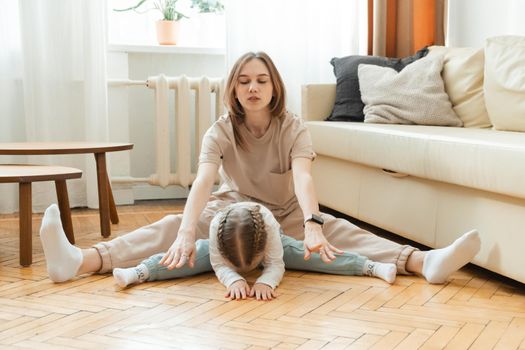 Beautiful young woman and cute little daughter doing stretching together at home. Healthy and sporty lifestyle