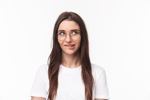 Close-up portrait of sassy and cute young brunette girl, biting lip tempting do something, having plan, look up thoughtful, standing white background, imaging or daydreaming. Copy space