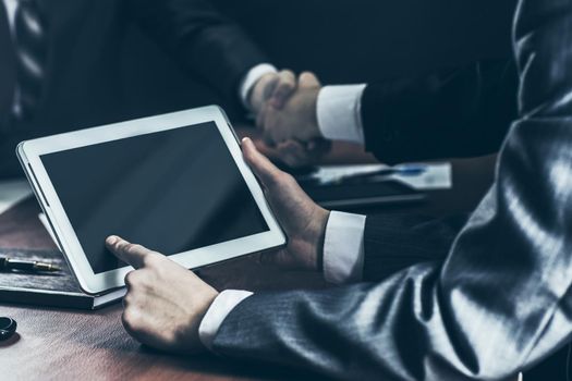 businessman with digital tablet in the background of handshake of business partners.photo on a black background and has space for your text.t