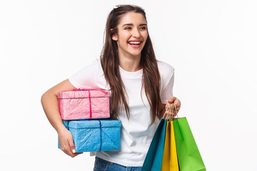 Shopping, holidays and lifestyle concept. Portrait of happy pleased young girl likes making presents and celebrating, holding wrapped bags of gists, laughing and walking to friend birthday.