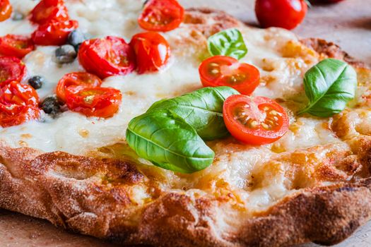 Small homemade vegetarian pizza with addition of tomatoes, capers on a wooden rustic table.