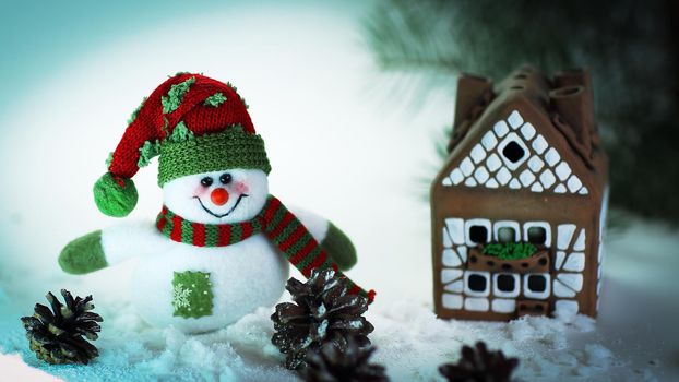 toy snowman and a gingerbread house on a light background. photo with copy space.