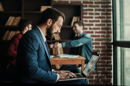 advertising Manager works with the marketing graphics on laptop on background of business partners handshaking in the workplace in the office