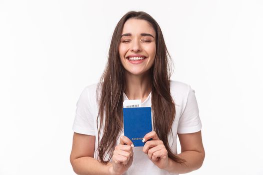 Travelling, holidays, summer concept. Close-up portrait of happy, dreamy girl feeling happy finally travel, holding passport with plane ticket, waiting in airport, standing white background.