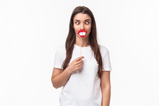 Entertainment, fun and holidays concept. Portrait of funny and joyful celebrating fools day april first, having fun, holding stick with lips and big teeth, show hilarious grimaces, white background.