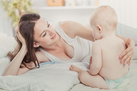 happy mother and year-old baby playing on bed in bedroom