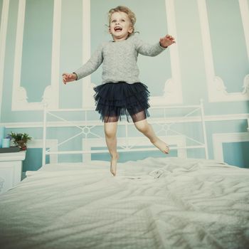 happy five year old girl jumping on the bed in the parents ' bedroom