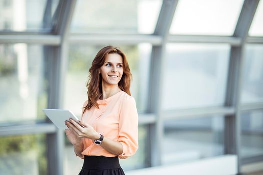 business woman with digital tablet standing near a large window in a modern office.the photo has a empty space for your text