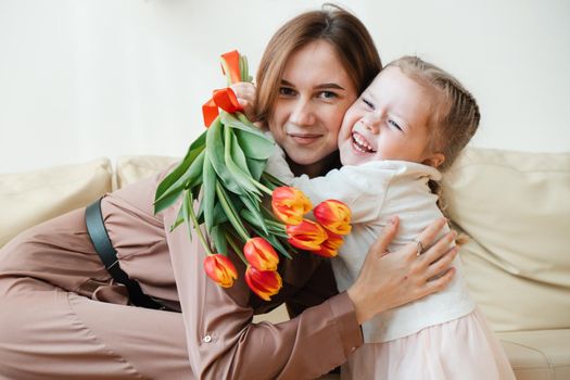 Postcard for March 8. Little daughter kisses and hugs mother with yellow flowers, tulips. Mothers Day.