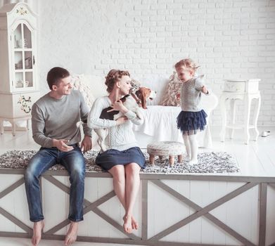 happy parents with five-year-old daughter and their pet dog in the cosy living room