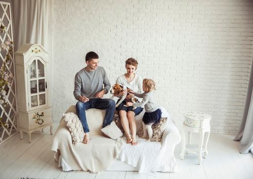 happy parents,five year old daughter with a pet dog sitting on the couch in the living room