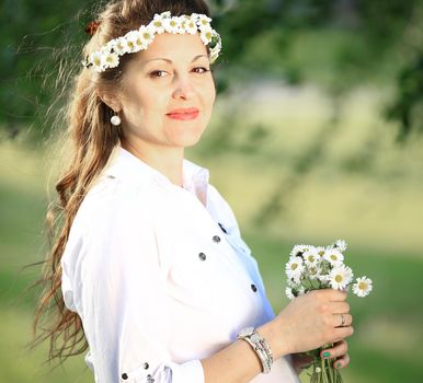 pregnant woman in a wreath and a bouquet of wild flowers on a walk in the Park on a Sunny day