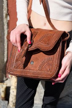 small brown women's leather bag with a carved pattern. street photo