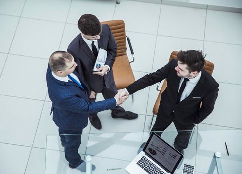 assistant with financial documents and business partners shake hands before starting a business meeting