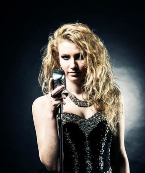 beautiful blonde woman singer in a black dress holding a microphone and sings a song.photo on dark background