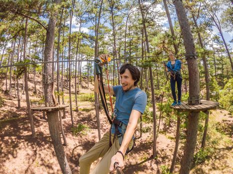 Young attractive man and woman in adventure rope park in safety equipment.