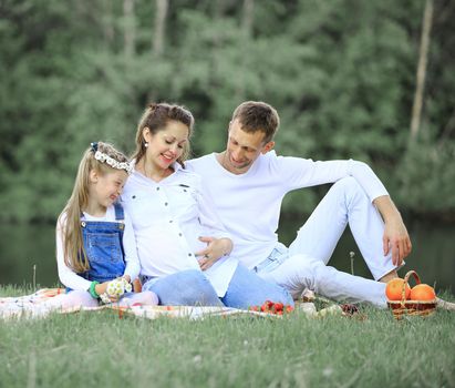 pregnant mother and happy father and little daughter at a picnic in the Park on a Sunny day. the photo has a empty space for your text