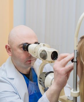 A male ophthalmologist checks the eyesight of a young girl using a modern device with a light beam.