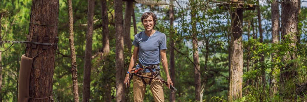 Young attractive man in adventure rope park in safety equipment. BANNER, LONG FORMAT