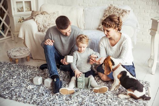 happy parents and five year old daughter playing with a pet dog in the spacious living room on Sunday