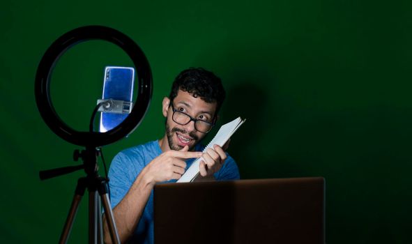 Young man with laptop making video blog, Young man creator contents with celphone, man with his laptop making video call with green background,