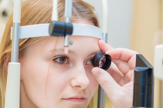 A male ophthalmologist checks the eyesight of a young girl using a modern device with a light beam.