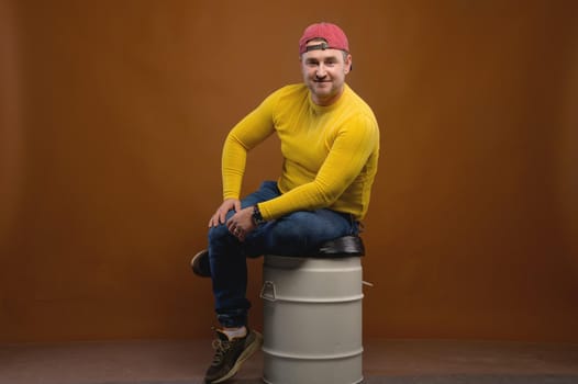 Portrait of an attractive friendly Caucasian man in a cap and yellow sweater on a brown background. Nice middle aged guy in casual clothes. Looks into the camera. Copy space.