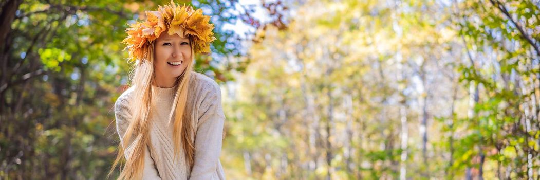 Outdoors lifestyle close up portrait of charming blonde young woman wearing a wreath of autumn leaves. Smiling, walking on the autumn park. Wearing stylish knitted pullover. Wreath of maple leaves. BANNER, LONG FORMAT