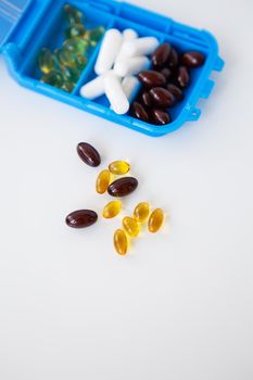 Spilling pills and capsules on a white background close-up together with a container for pills. Top view with copy space. Medicine concept