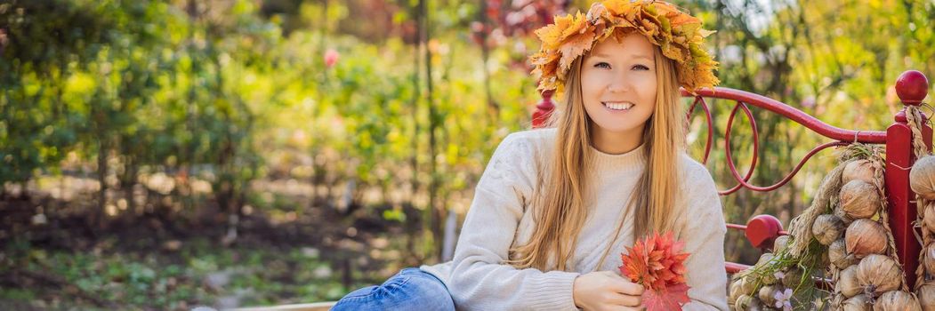 Outdoors lifestyle close up portrait of charming blonde young woman wearing a wreath of autumn leaves on a haystack. Wearing stylish knitted pullover. Wreath of maple leaves. BANNER, LONG FORMAT