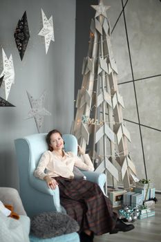 young woman sitting in a chair near a stylized Christmas tree. holiday concept